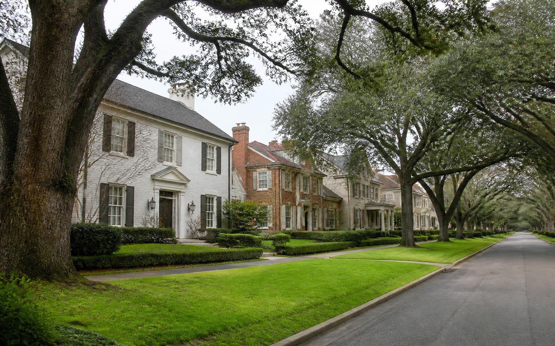 Row of varied brick and painted-brick houses set behind deep lawns on a tree-lined Myers Park street