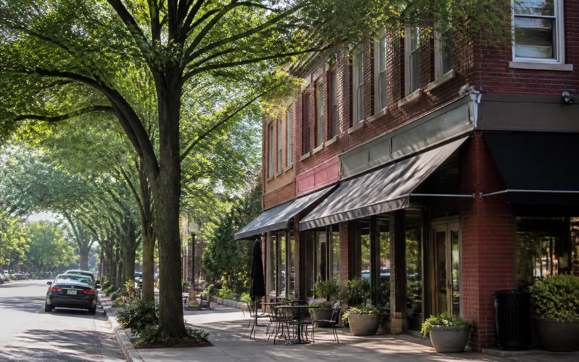 Brick storefront row with awnings and sidewalk cafe tables under street trees on Selwyn Avenue, Charlotte