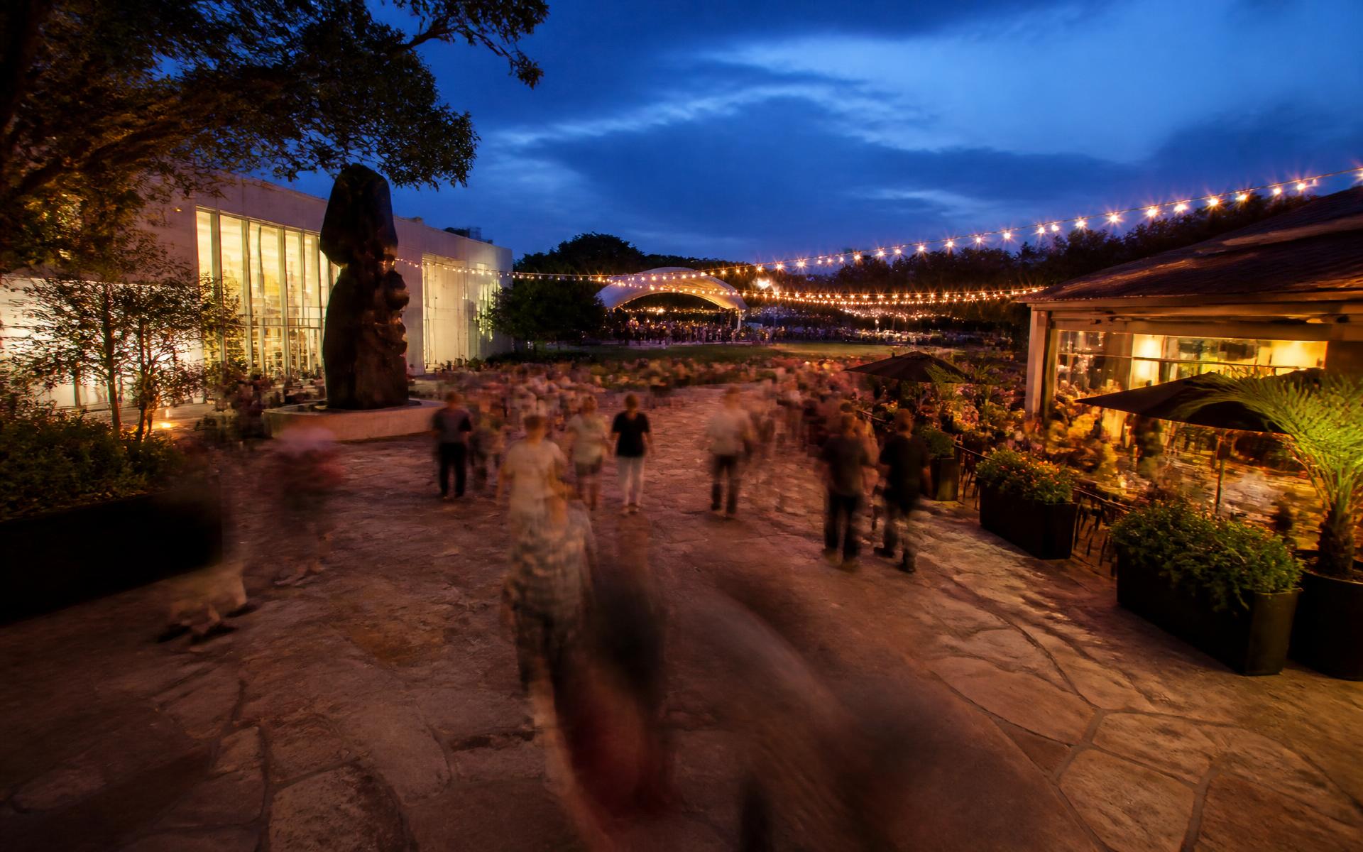 Outdoor cultural plaza in Charlotte at dusk with string lights and an amphitheater lawn